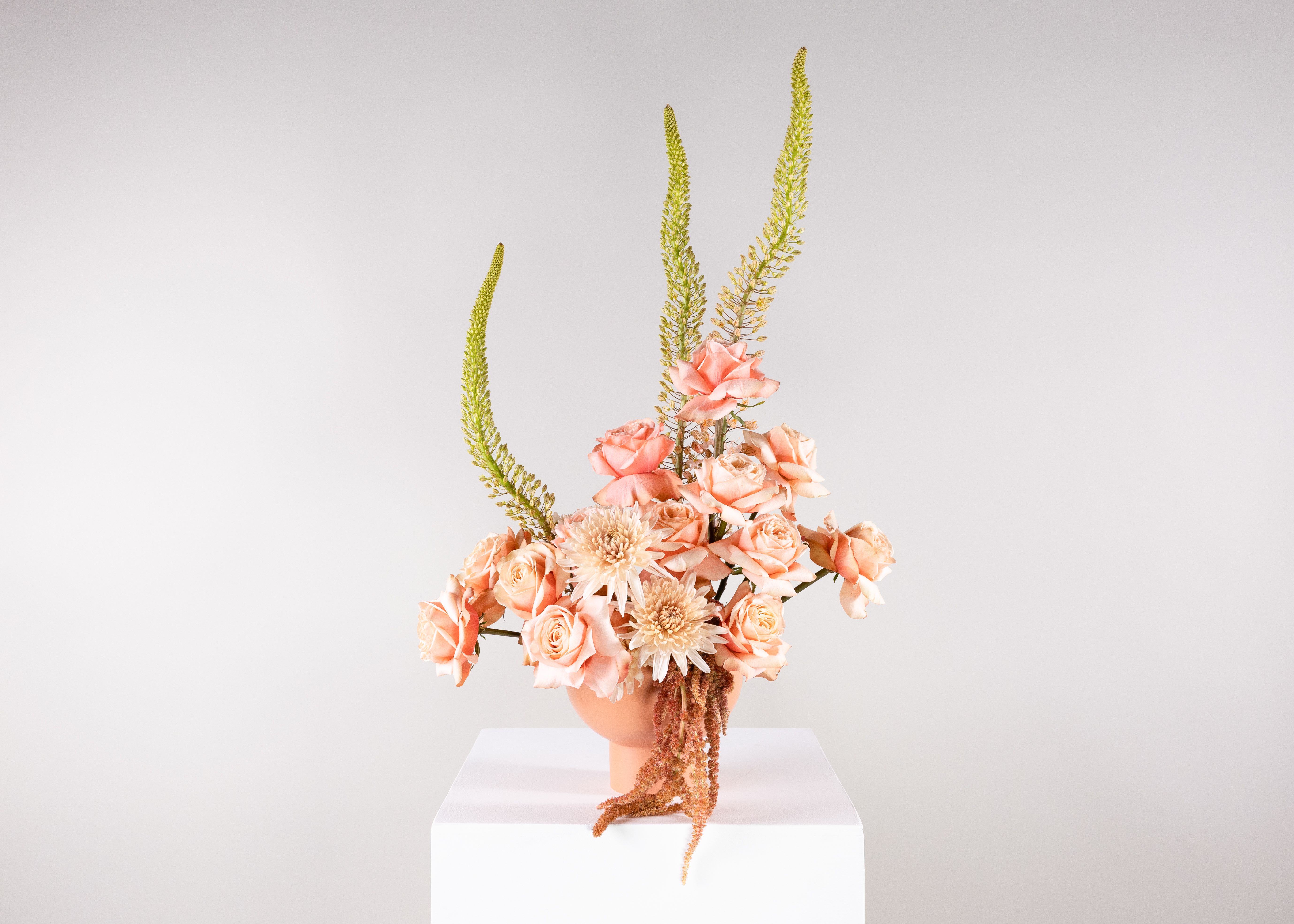 Peach roses and pale blooms in a peach vase with tall green spikes
