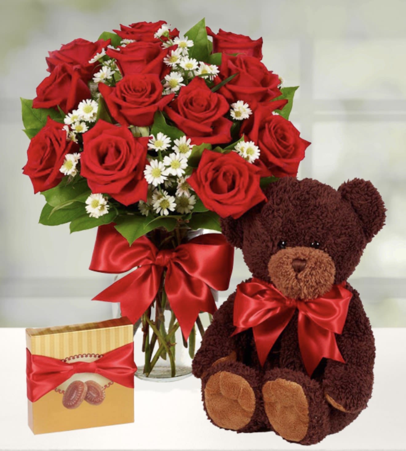 Bouquet of red roses in a glass vase with a teddy bear and chocolate box
