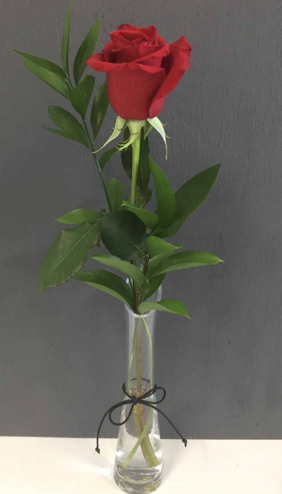 Single red rose in a clear glass vase with greenery