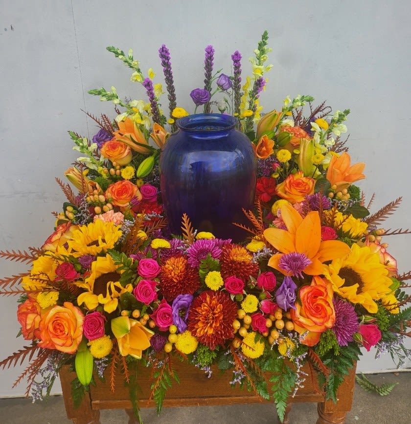 Colorful floral arrangement around a blue urn on a wooden stand