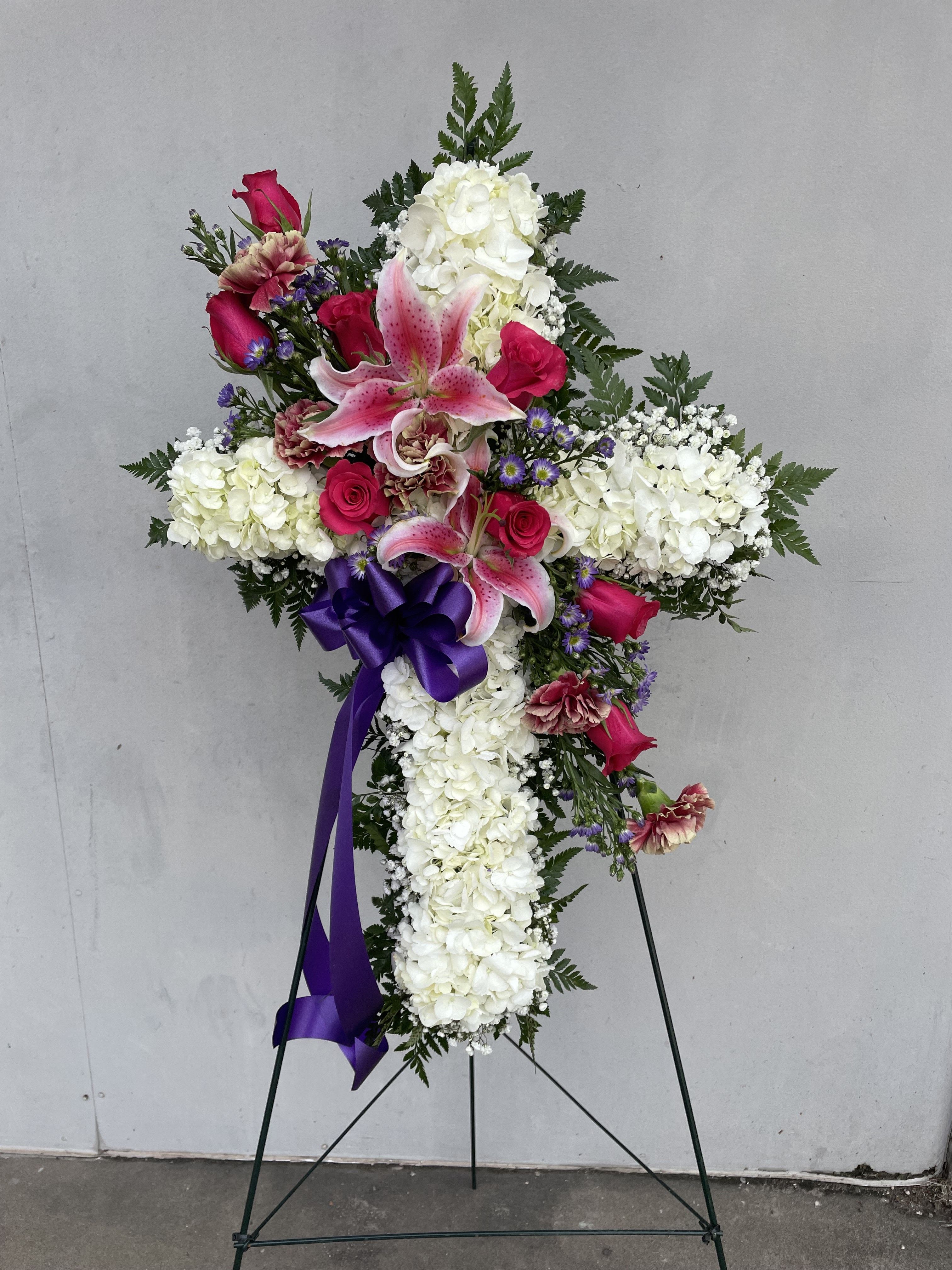 Cross-shaped floral funeral spray with white hydrangeas, pink lilies, and roses