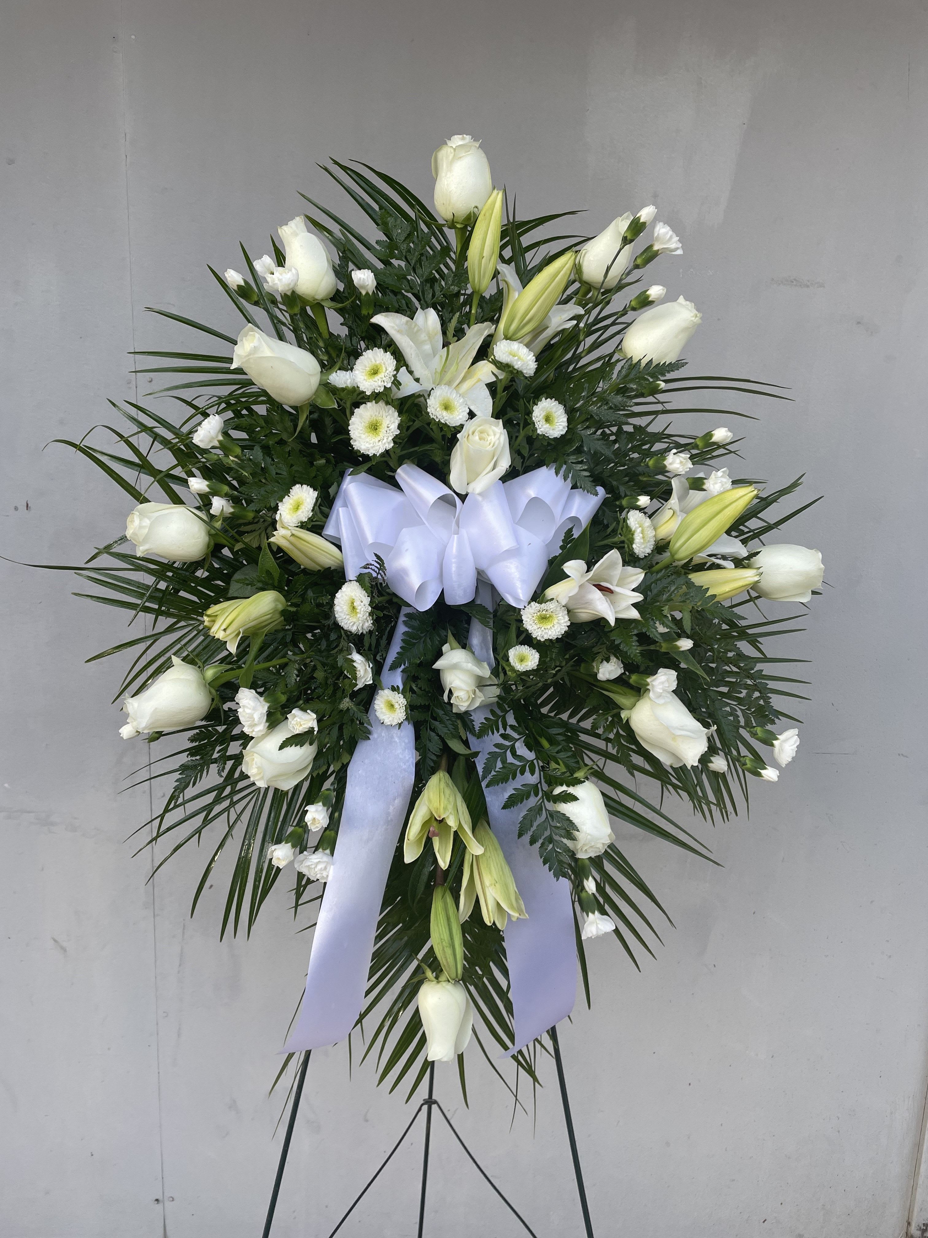 White floral standing spray with lilies and roses on a ribboned easel