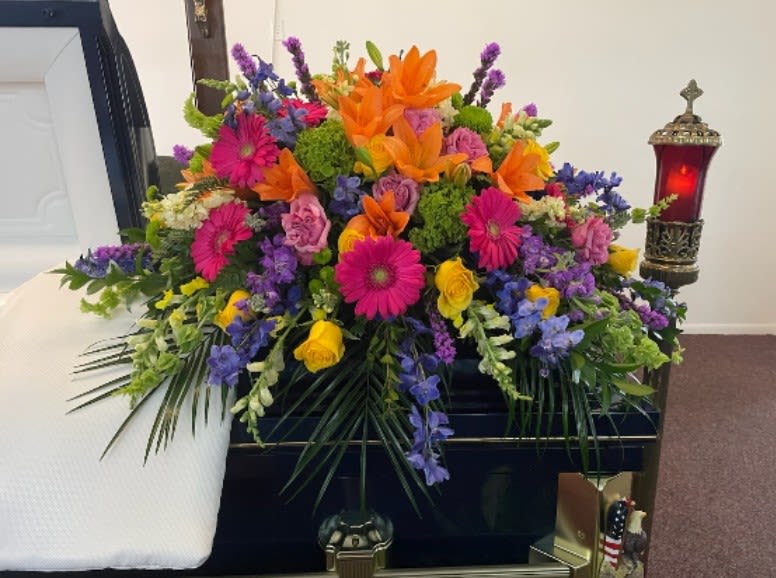 Colorful funeral spray with orange lilies, pink daisies, and purple flowers