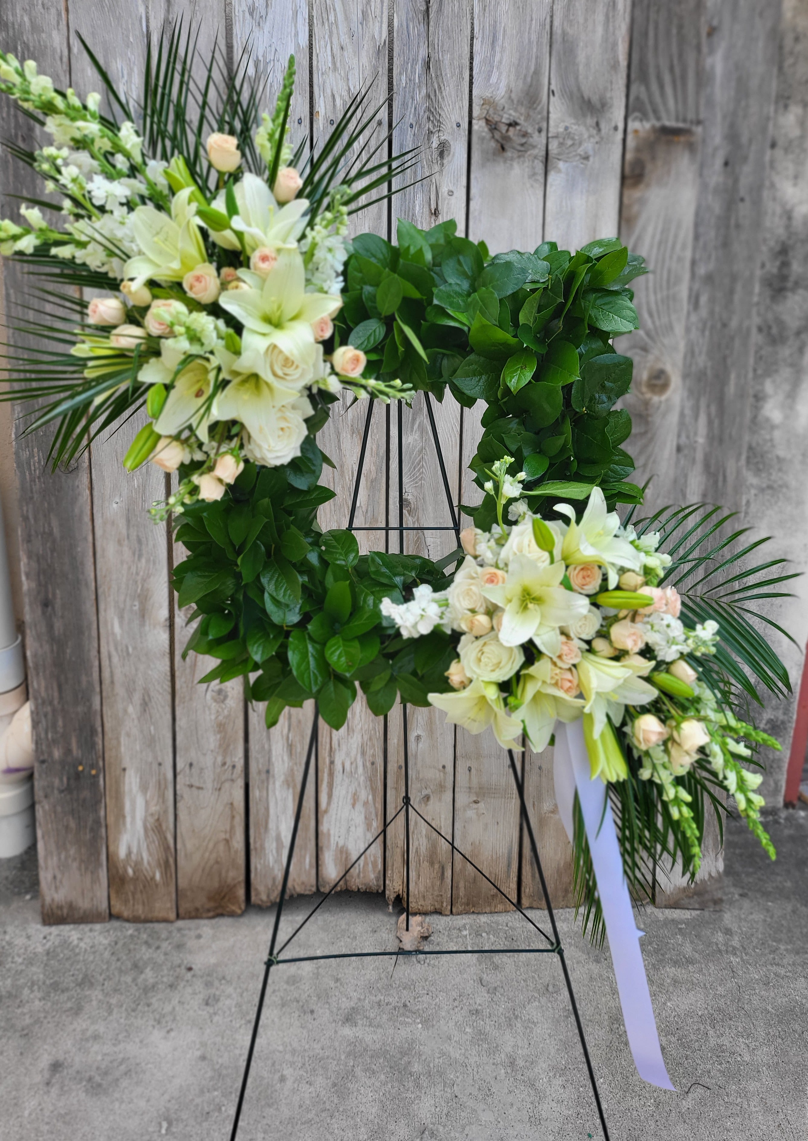 Large floral wreath on a stand with white lilies and pale roses