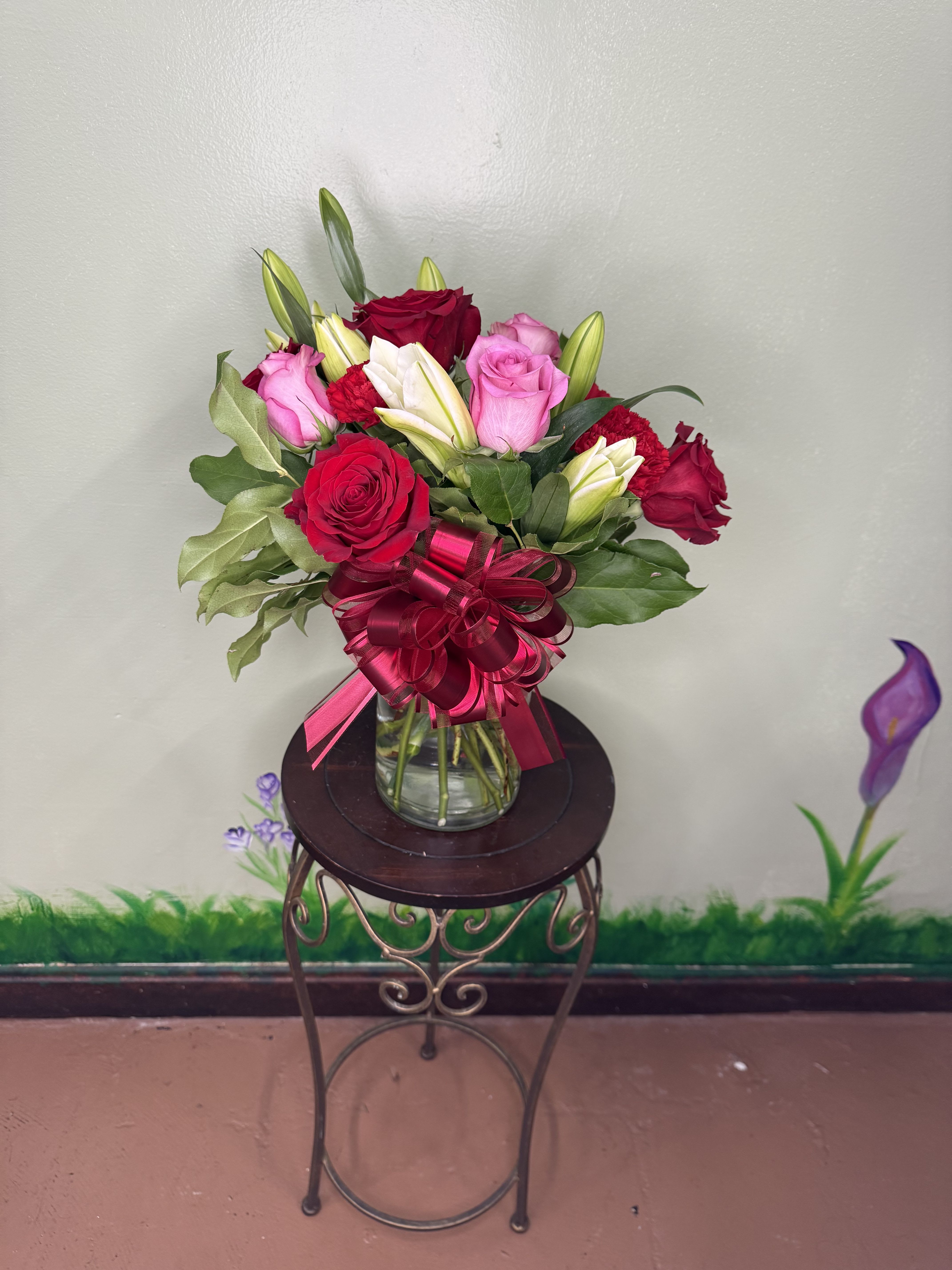 Mixed bouquet of red and pink roses with white lilies in a clear glass vase with a red bow.