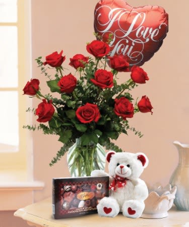 Red roses in a vase with a heart balloon, teddy bear, and chocolates