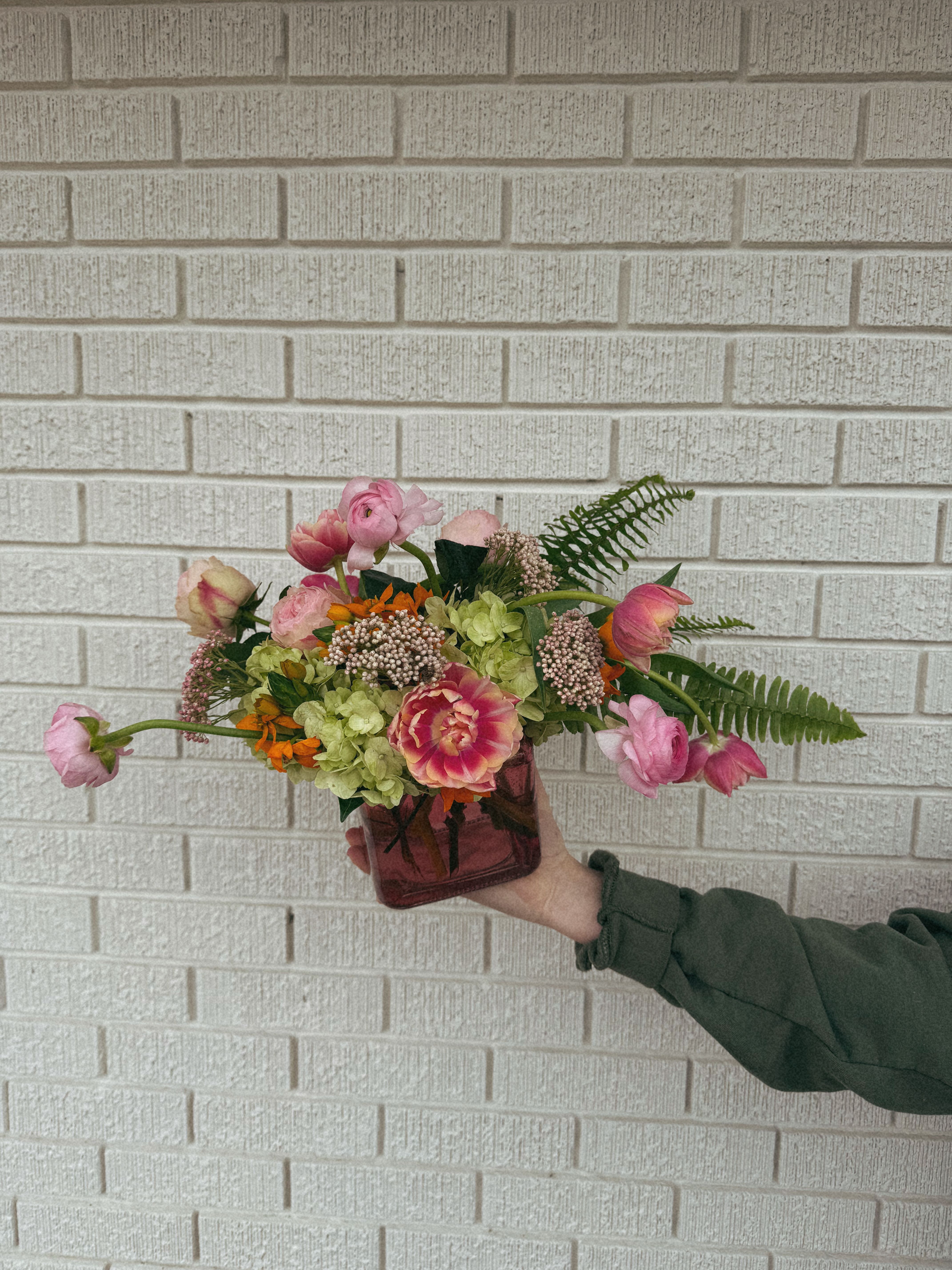 Handheld bouquet in a square glass vase with pink and green flowers