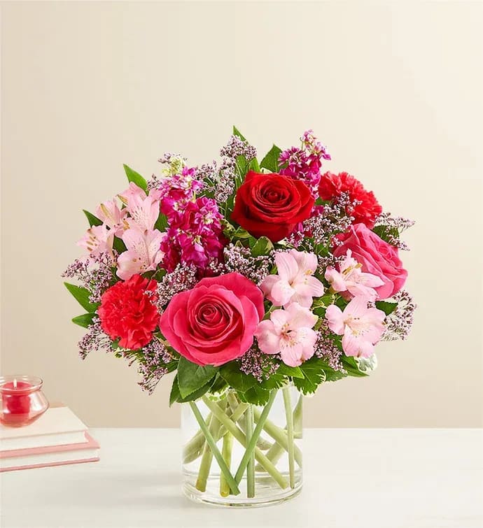 Floral Fantasy Bouquet - All-around arrangement with red roses, hot pink roses &amp; carnations, pink Peruvian lilies (alstroemeria) and Limonium, fuchsia stock; accented with assorted greenery Artistically designed in a clear glass cylinder vase; extra large/large measures 6"; medium/small measures 5" Premium arrangement measures approximately 16"H x 12"W, comes in 6" cylinder Deluxe arrangement measures approximately 15"H x 11"W, comes in 6" cylinder  ; Standard  measures approximately 13"H x 10"W, comes in 5" cylinder 