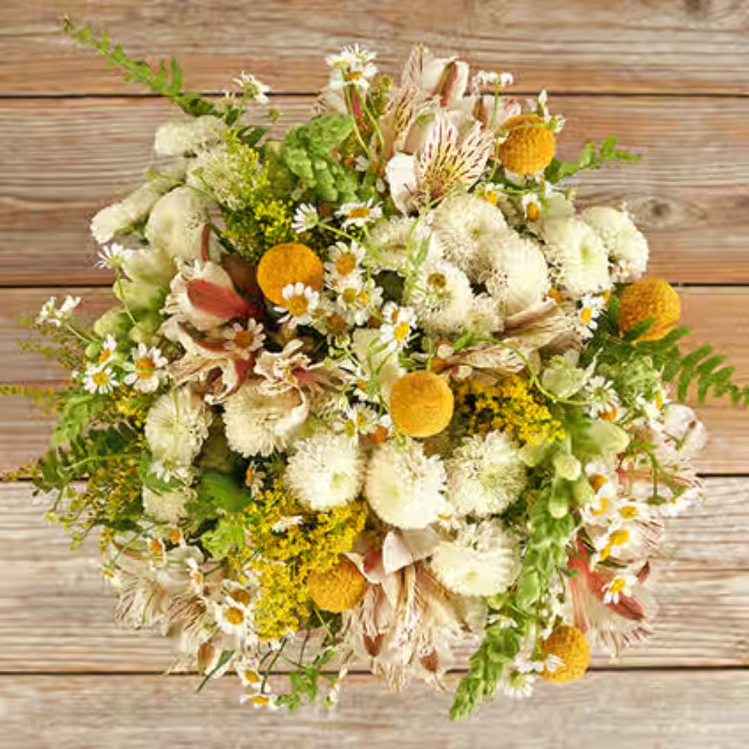 Mixed bouquet of white and yellow flowers with green accents on a wood surface