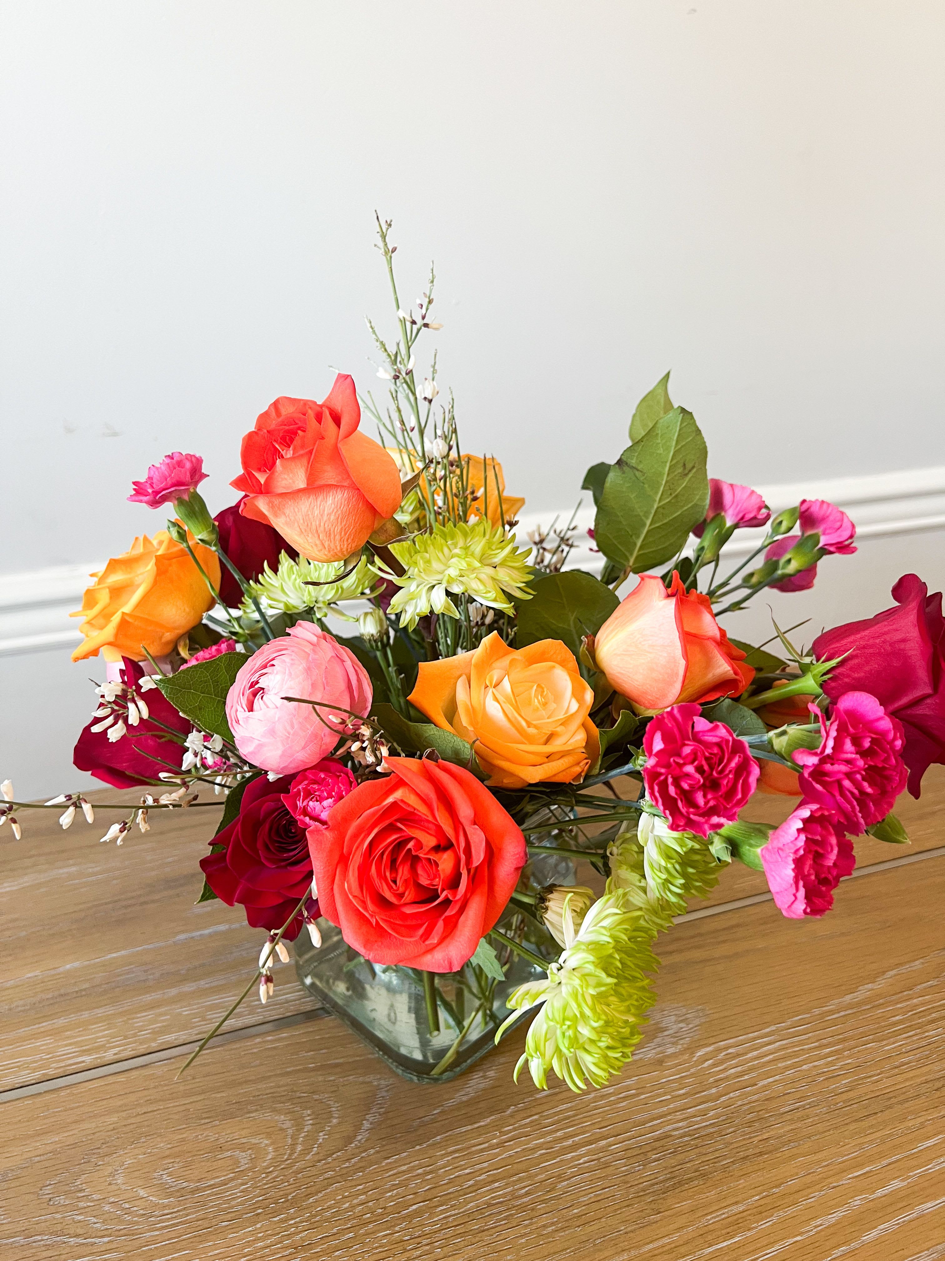 Mixed bouquet of roses, carnations, and mums in a glass vase