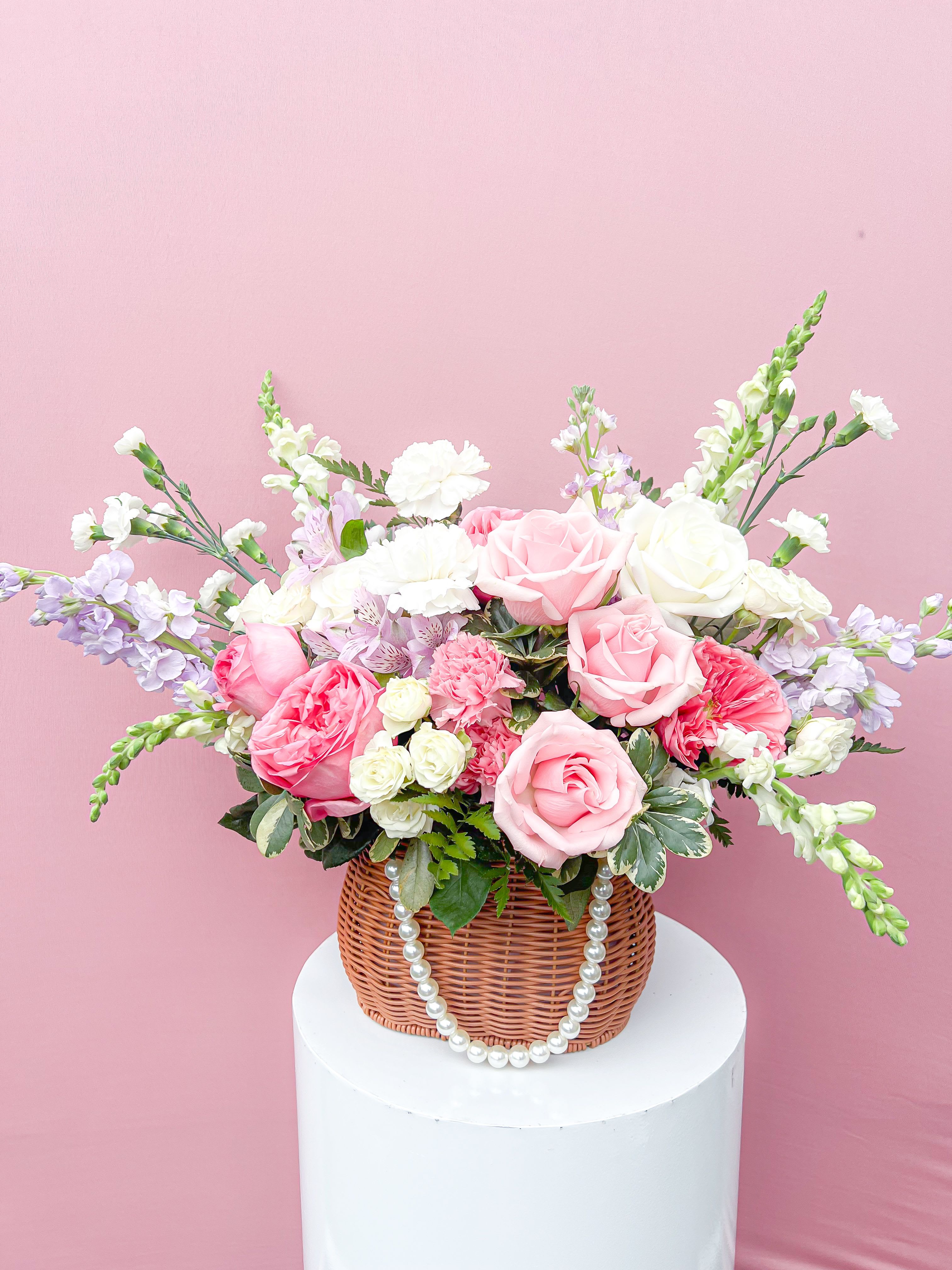 Pink and white rose arrangement in a wicker basket with pearl trim