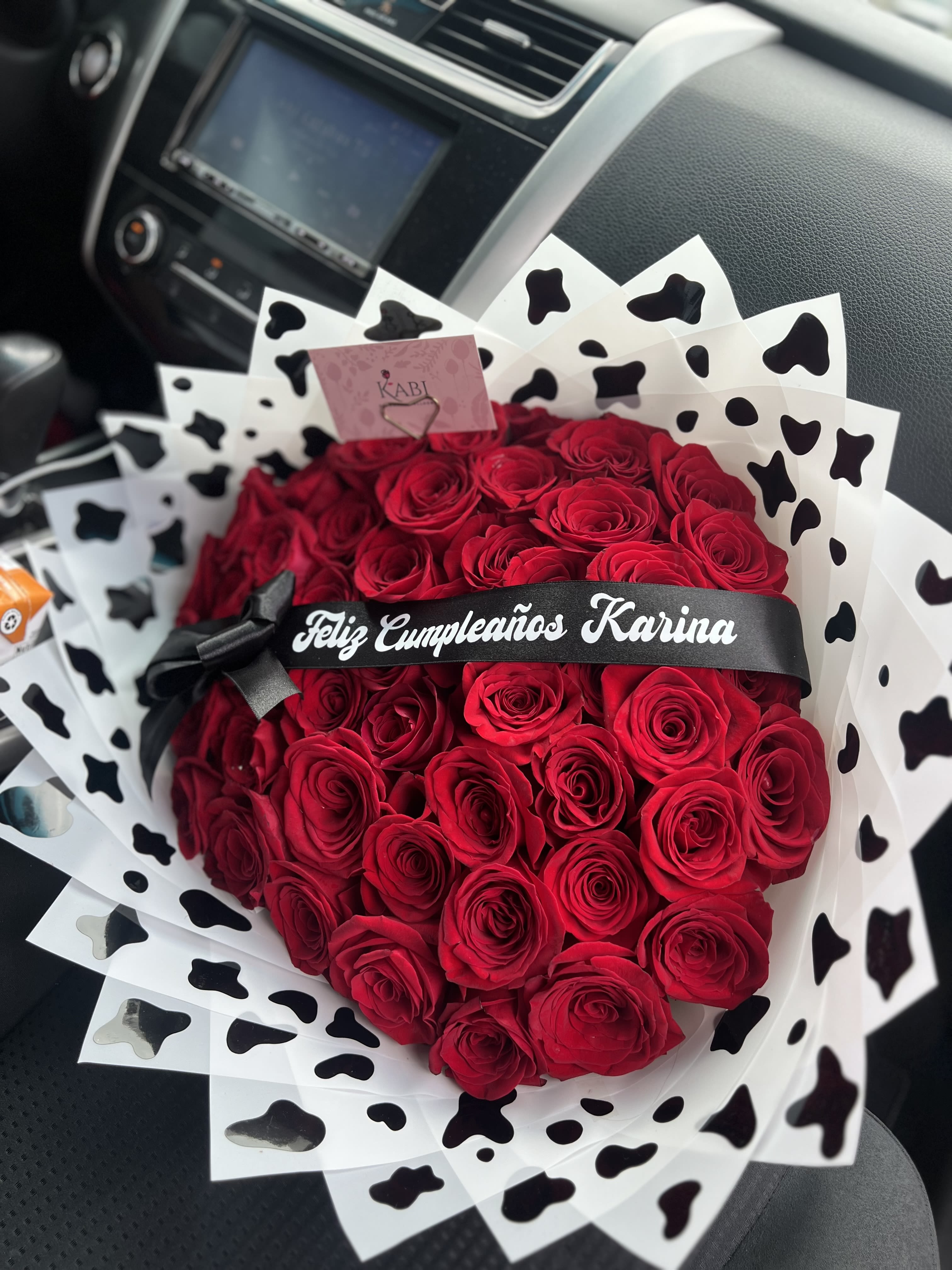 Heart-shaped bouquet of red roses with black-and-white wrap and ribbon
