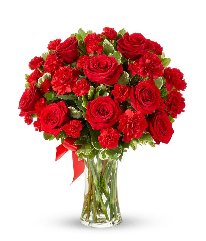 Red roses and carnations in a clear glass vase with a red ribbon