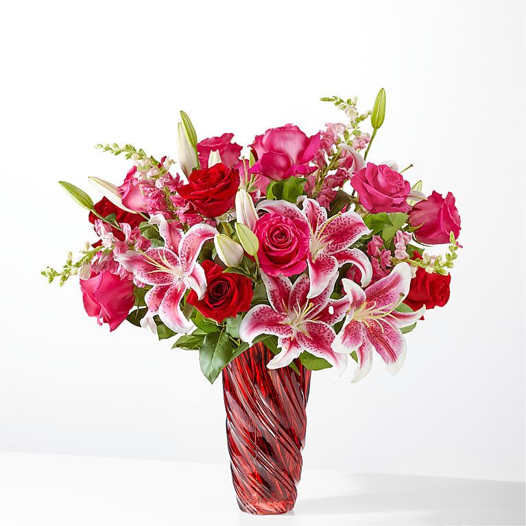 Pink and red roses with stargazer lilies in a red glass vase