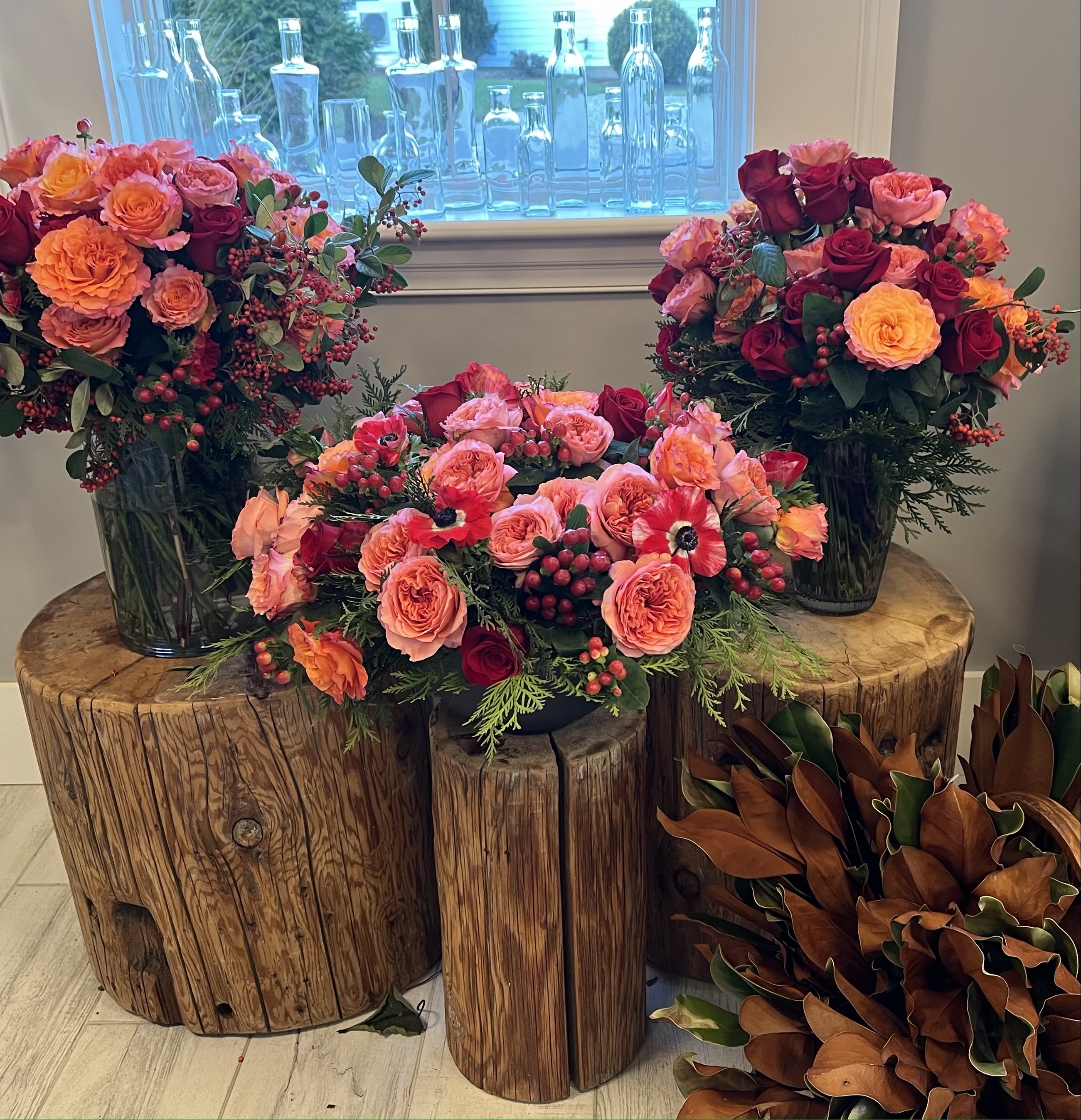 Three rose arrangements in dark glass vases on wooden stumps