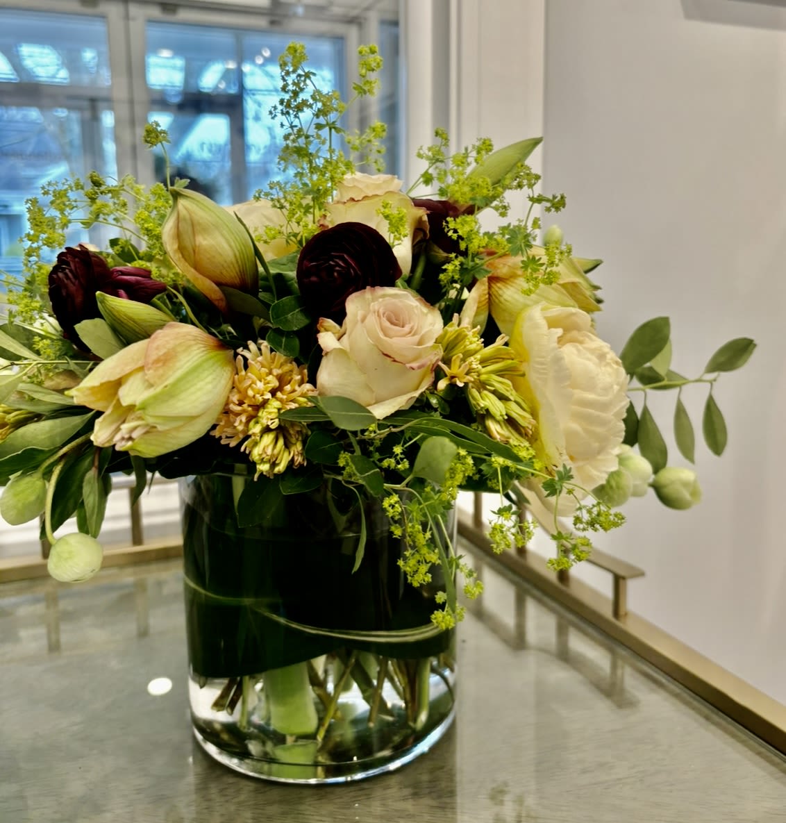 Dream in Winter - Amaryllis, roses, ranunculus, hellebore, and hyacinth in shades of cream, peach and burgundy in a clear glass vase. 