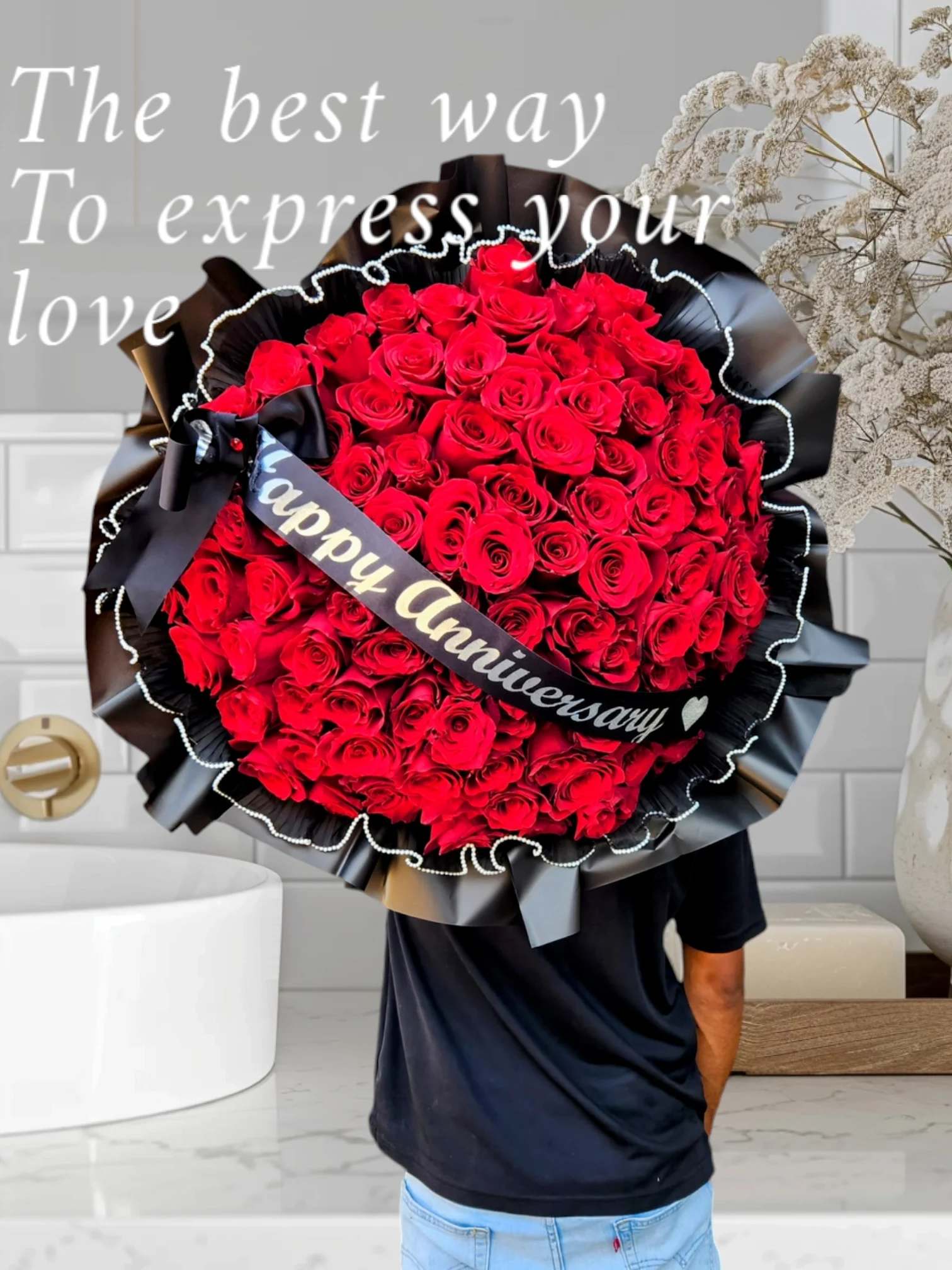 Large bouquet of red roses wrapped in black paper with a "Happy Anniversary" ribbon