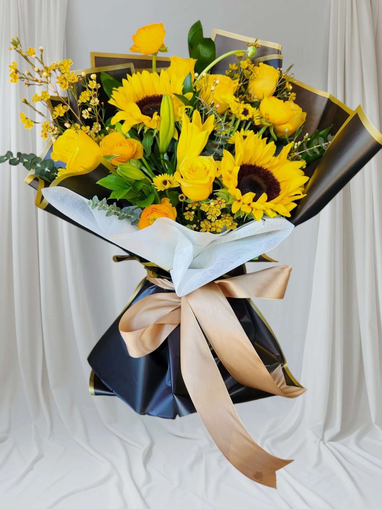 Bouquet of yellow flowers wrapped in black paper with a gold ribbon