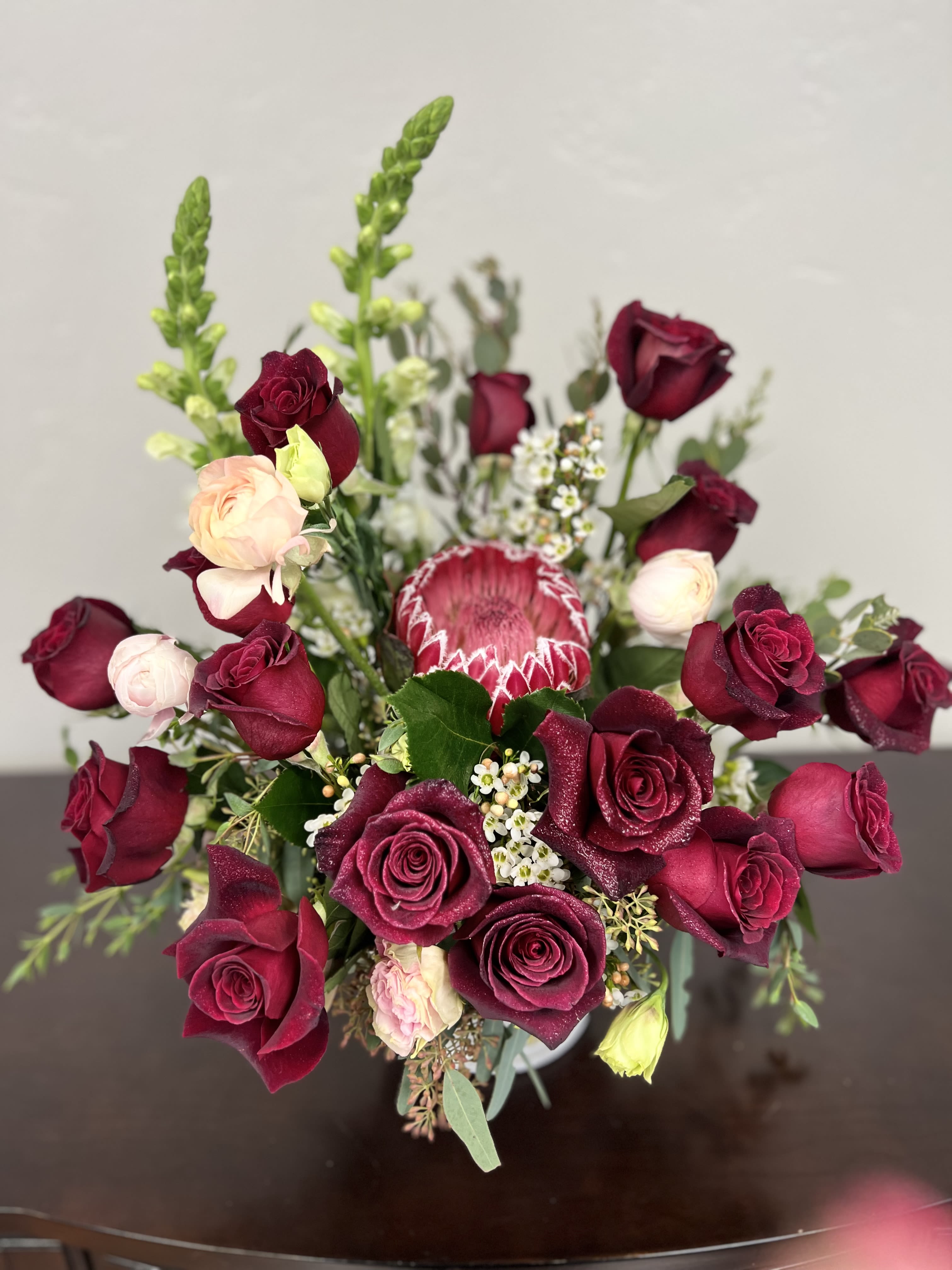 Bouquet of deep red roses with a pink protea and small white filler flowers