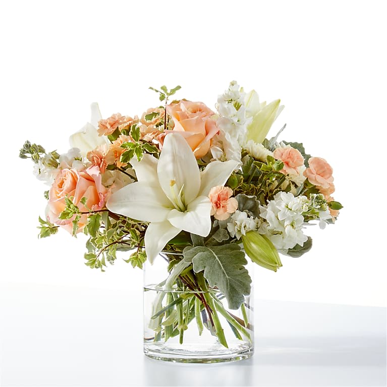 Peach roses and white lilies in a clear glass vase