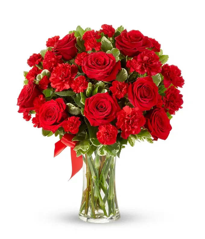 Red roses and carnations in a clear glass vase with a red ribbon