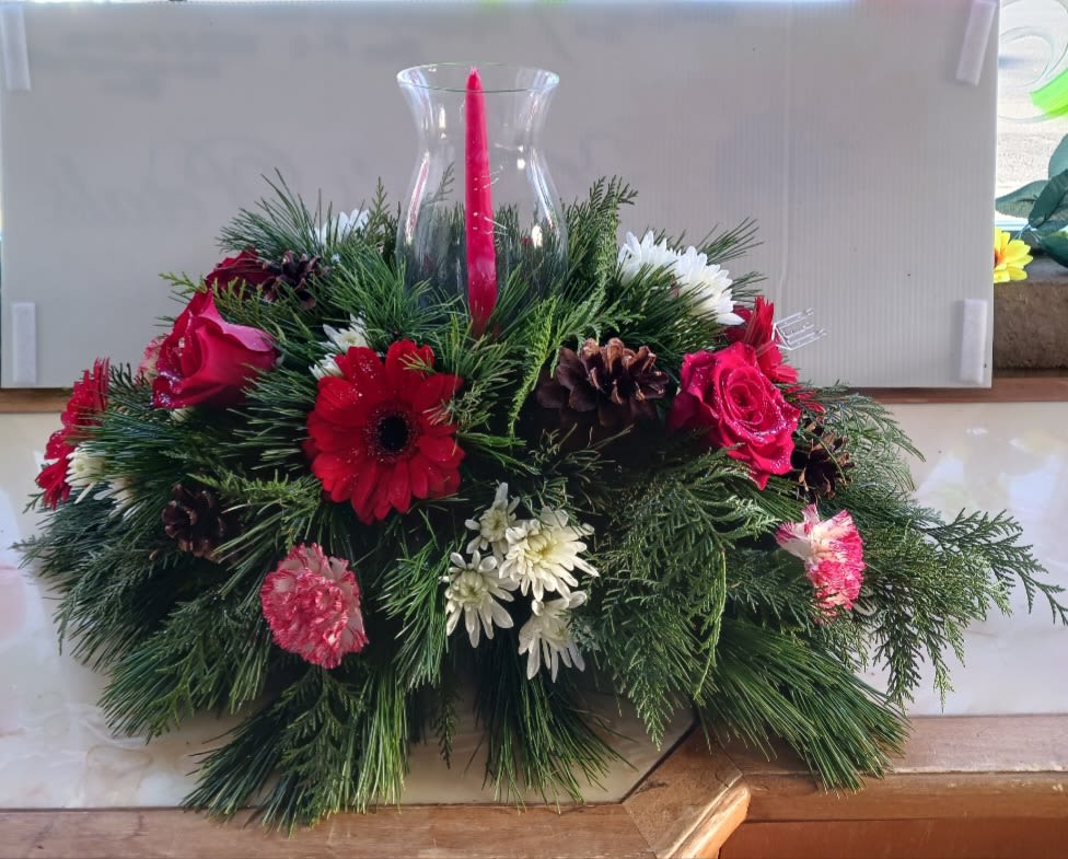 Holiday floral centerpiece with red and white flowers around a red candle in a glass vase