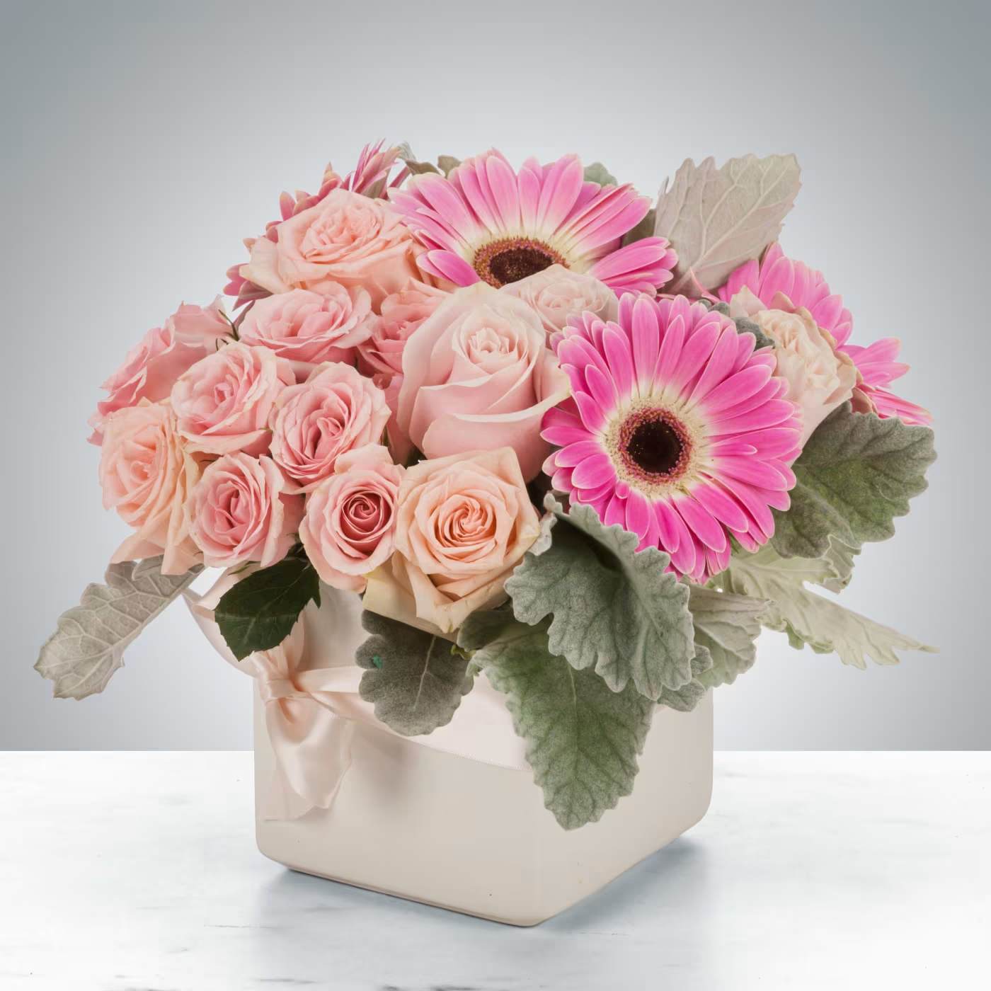 Pink roses and gerbera daisies in a cream square vase