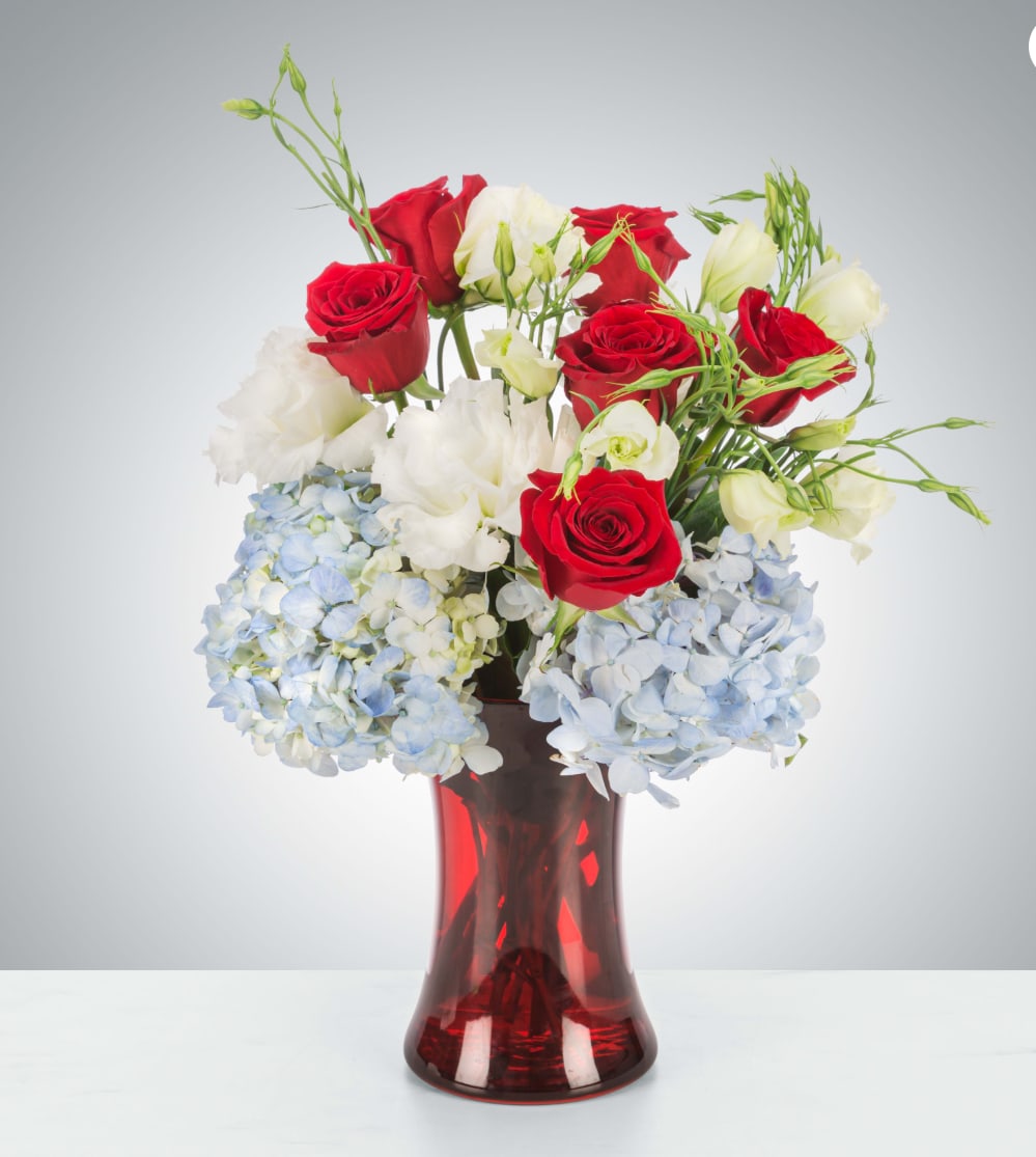 Red and white roses with blue hydrangeas in a red glass vase