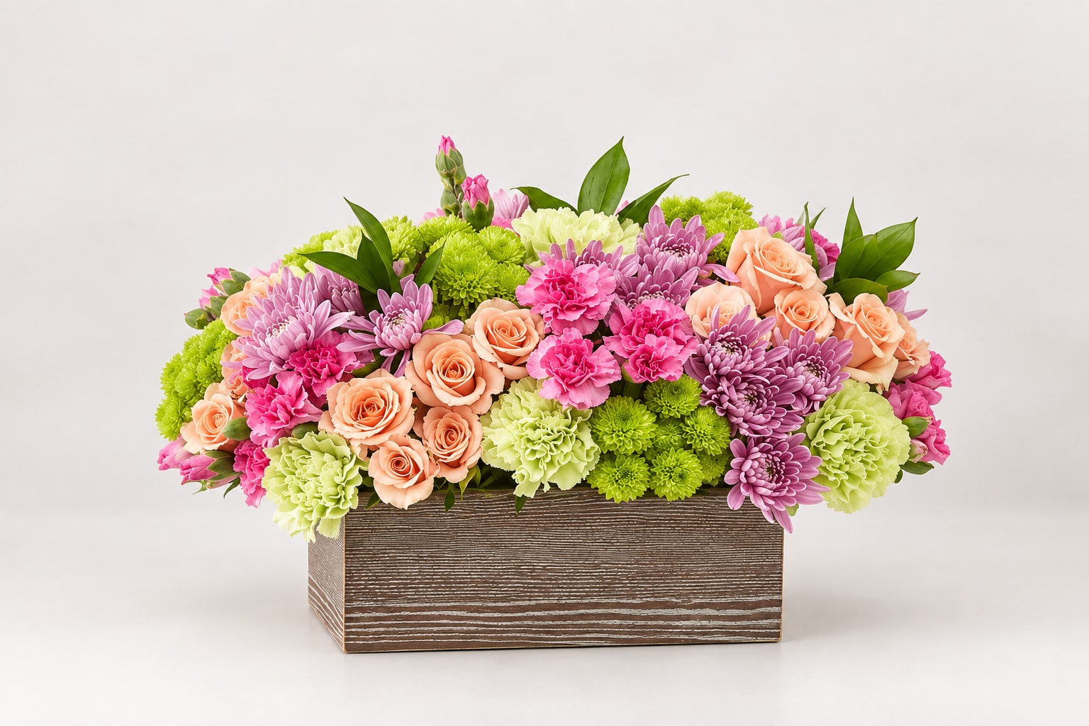 Mixed bouquet of pink, peach, and green flowers in a wooden box