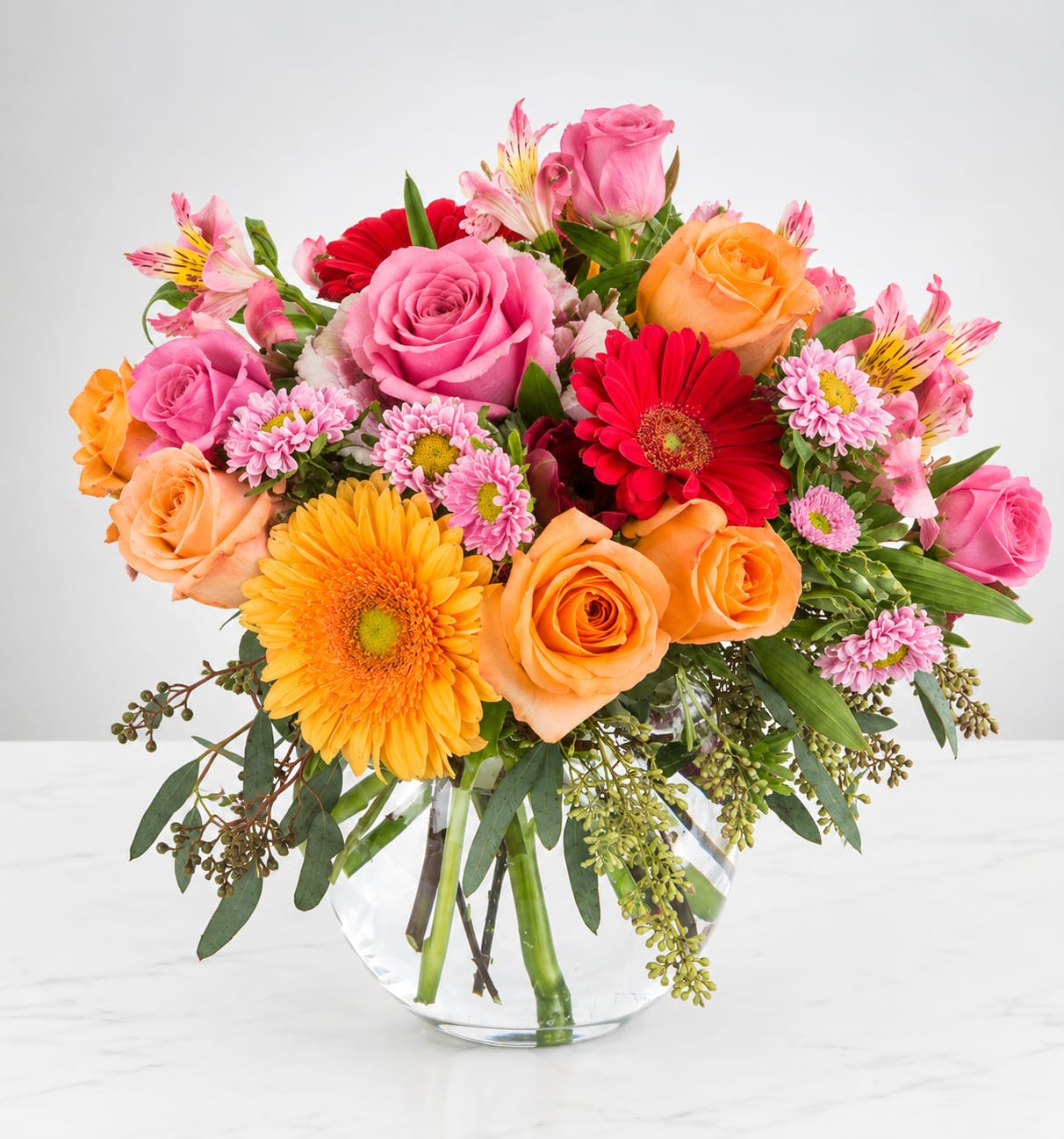 Mixed bouquet of pink, orange, and red flowers in a clear glass vase