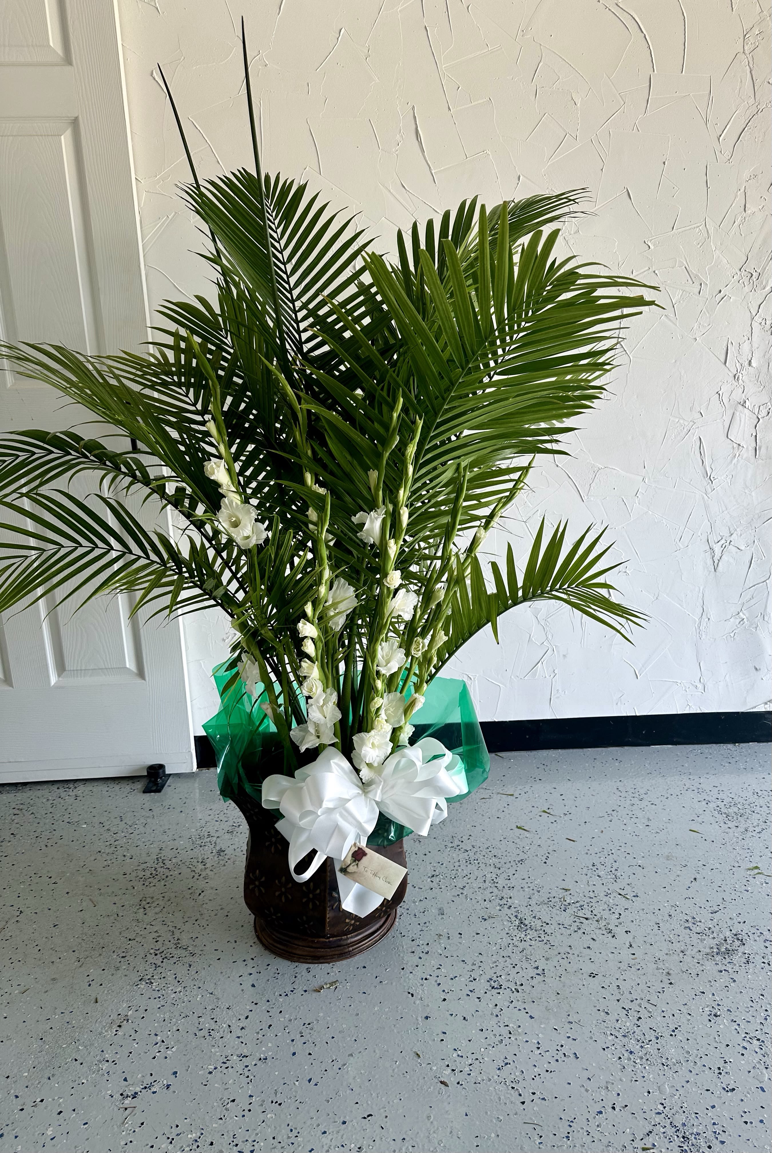 Tall palm plant arrangement with white flowers in a dark pot with white bow