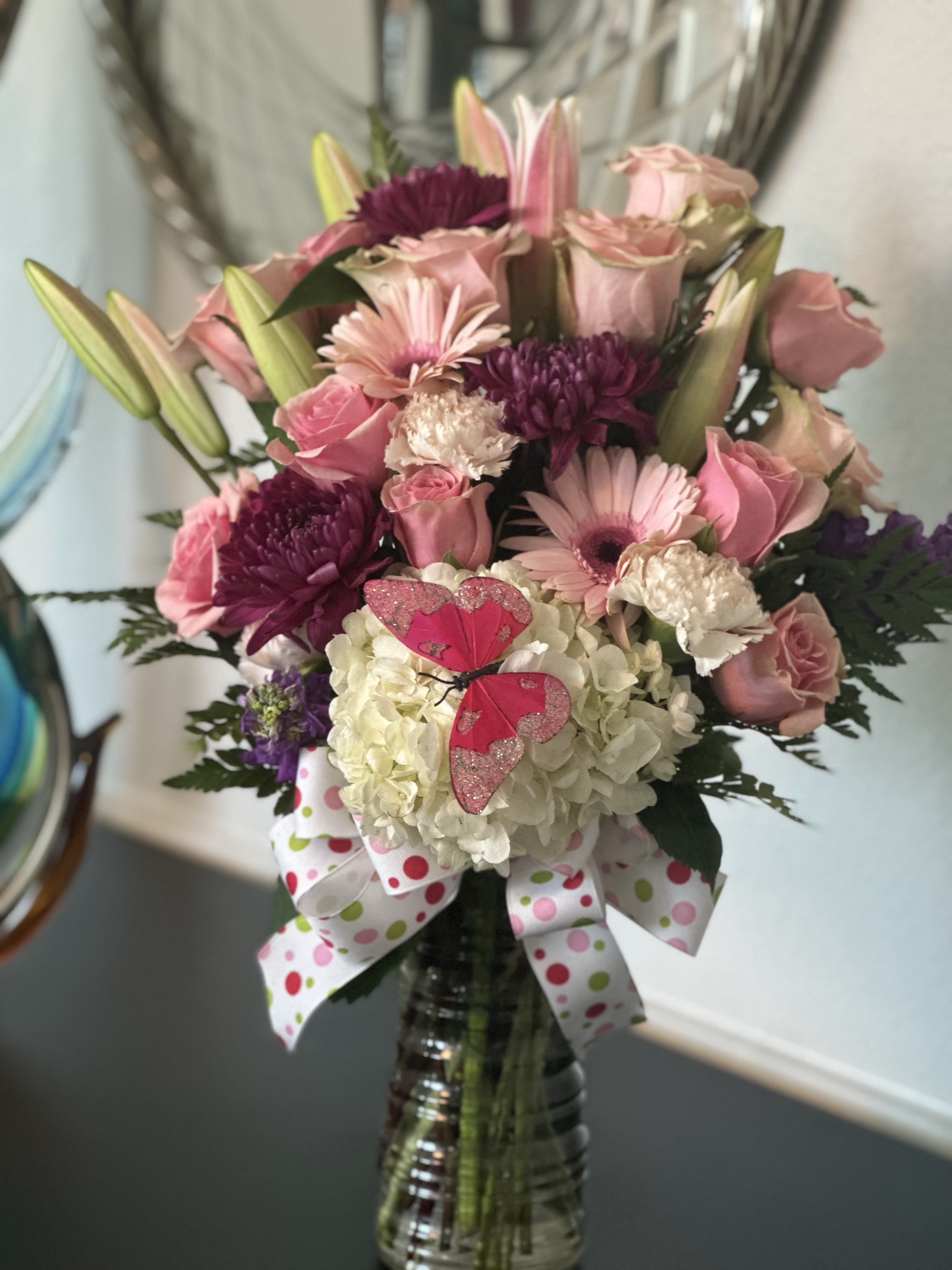 Tall pink and white mixed flower arrangement in a glass vase with ribbon and butterfly decoration