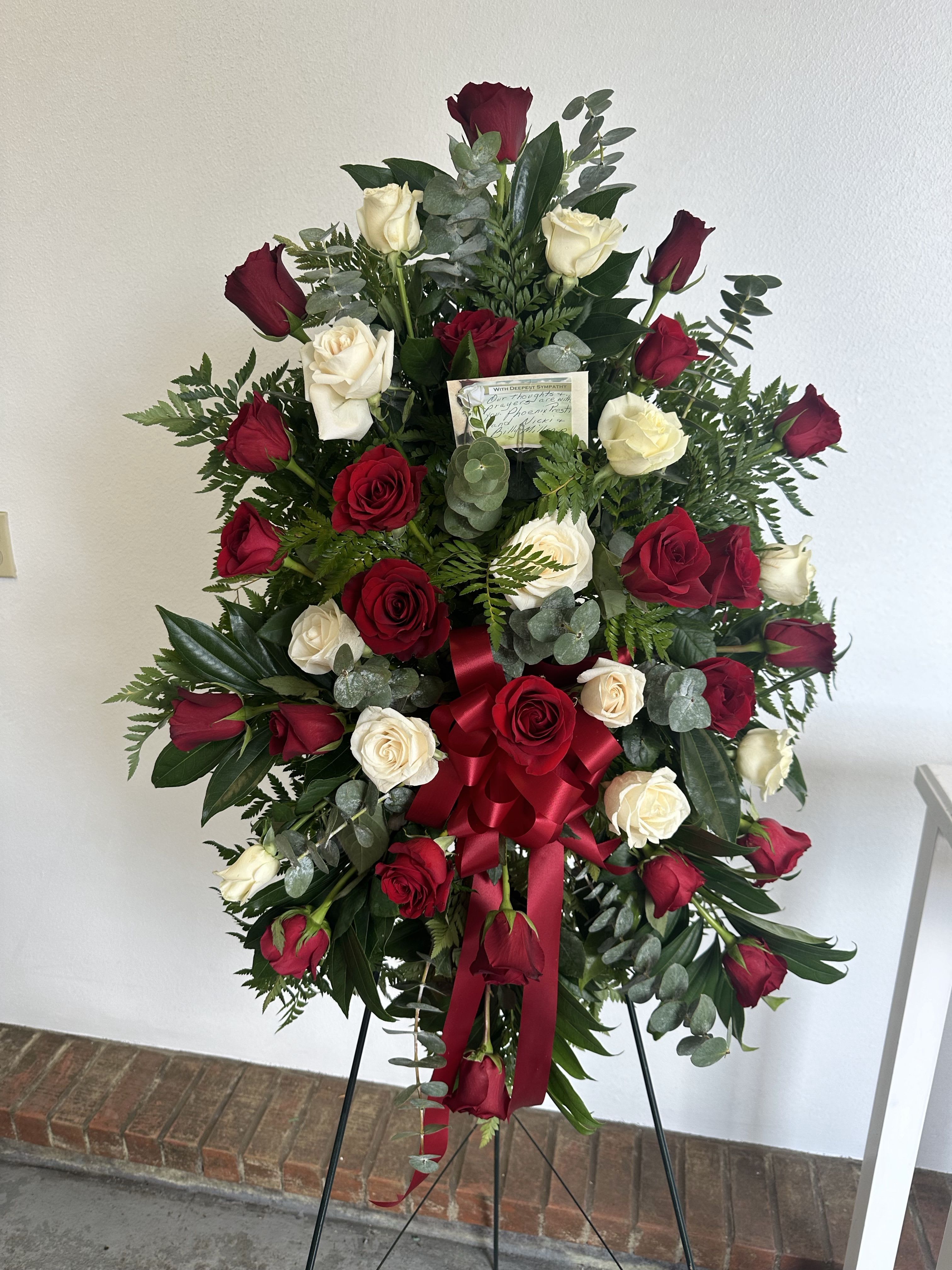 Standing spray of red and white roses with a red bow on a metal easel