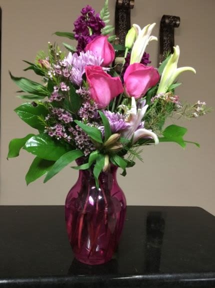 Pink and white mixed flower arrangement with roses and lilies in a bright pink glass vase