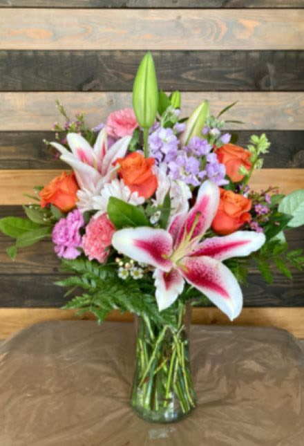 Tall mixed bouquet with pink lilies, orange roses, pink carnations and white daisies in a glass vase