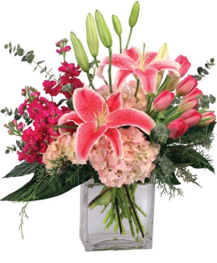Pink lilies, hydrangeas, and tulips arranged in a clear rectangular glass vase