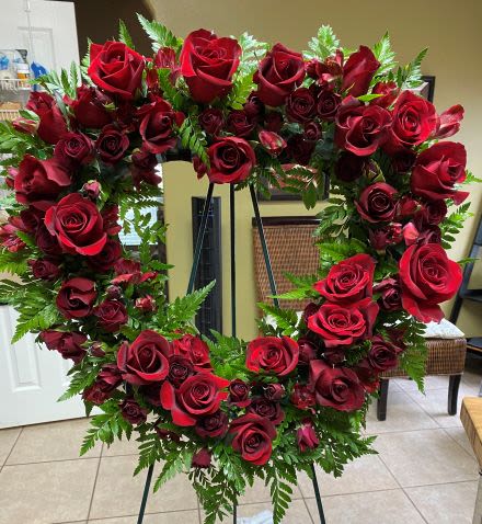 Heart-shaped wreath of red roses with abundant ferns on a standing easel