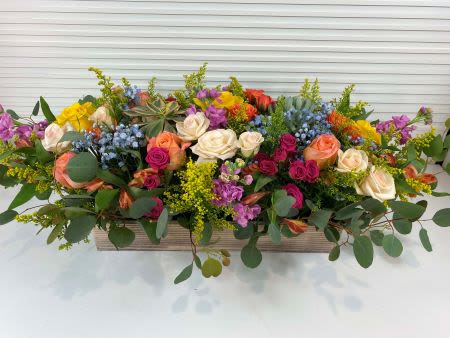 Long low arrangement of mixed roses and colorful blooms in a rectangular wooden box