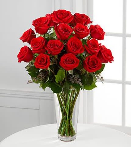 Tall clear vase filled with long-stemmed red roses.