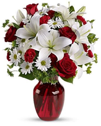 Arrangement of white lilies, red roses, red carnations, and white daisies in a red glass vase