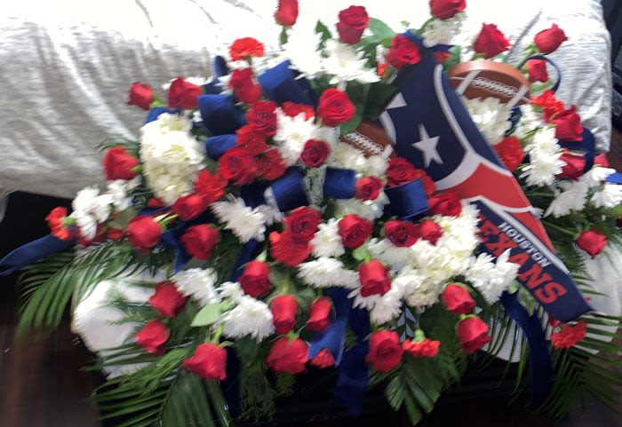 Red and white funeral spray with blue ribbon and Houston Texans logo on a casket