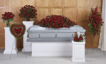 Funeral casket surrounded by red rose arrangements and a heart-shaped wreath with green border