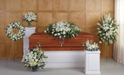 Set of white funeral flower arrangements surrounding a wooden casket in a chapel setting