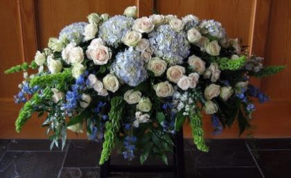 Large white rose and blue hydrangea spray with Bells of Ireland arranged on a stand
