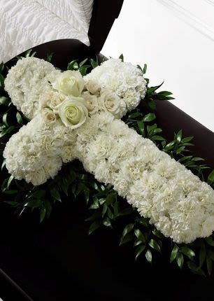 White floral cross arrangement with roses and carnations on a dark casket