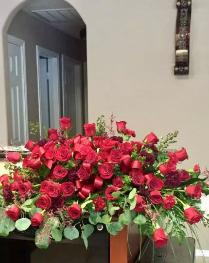 Large spray of red roses with dark red blooms and red ribbon arranged in a low, wide display