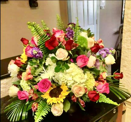 Large mixed arrangement of roses, hydrangea, sunflower and other blooms in a low container