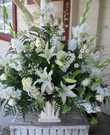 Tall all-white arrangement with lilies, roses, and snapdragons in a white pedestal vase