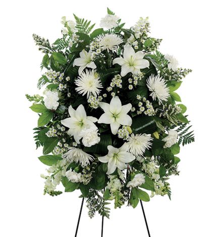 Standing spray of white lilies, carnations, and mums with small white fillers and lush greenery on an easel.