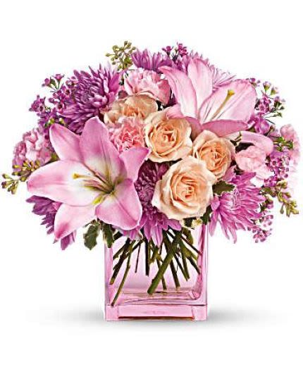 Pink and peach lilies, roses, and mums arranged in a pink glass cube vase